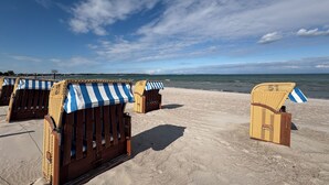 Strandstühle mit gestreifter Markise an einem Sandstrand mit Blick aufs Meer.
