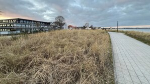 Ein Küstenwanderweg mit gepflastertem Pfad, Grünflächen und Gebäuden im Hintergrund.