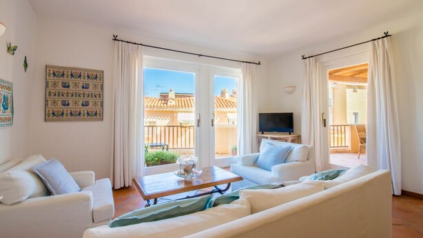 Una sala de estar con un sofá, una mesa de centro y un televisor. Hay cortinas y un ventanal con vistas a edificios.