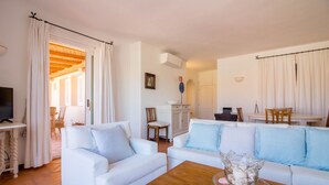 Una sala de estar con sofás blancos, una mesa de centro de madera y un televisor.