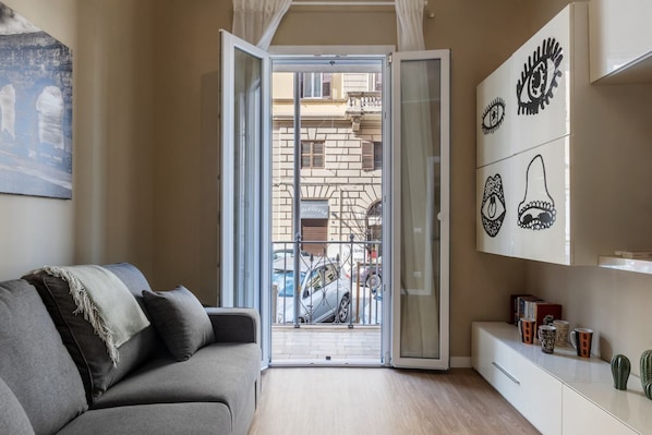 A living room with a grey sofa, a glass door leading outside, and a wall with decorative eye patterns.