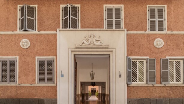 A building facade with a central entrance, multiple windows with shutters, and decorative elements above the doors.