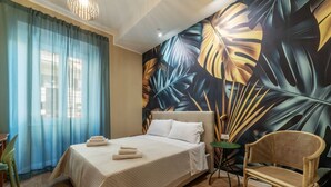 A hotel room with a bed, a chair, a small table, and a large wall mural.