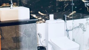 Un bagno moderno con rivestimento in marmo, uno specchio rotondo, un lavandino bianco, un WC e uno spazio doccia.