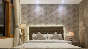 Una camera da letto con testiera trapuntata, letto con lenzuola bianche, due cuscini decorativi, un comodino con una lampada e una parete con carta da parati a fantasia.