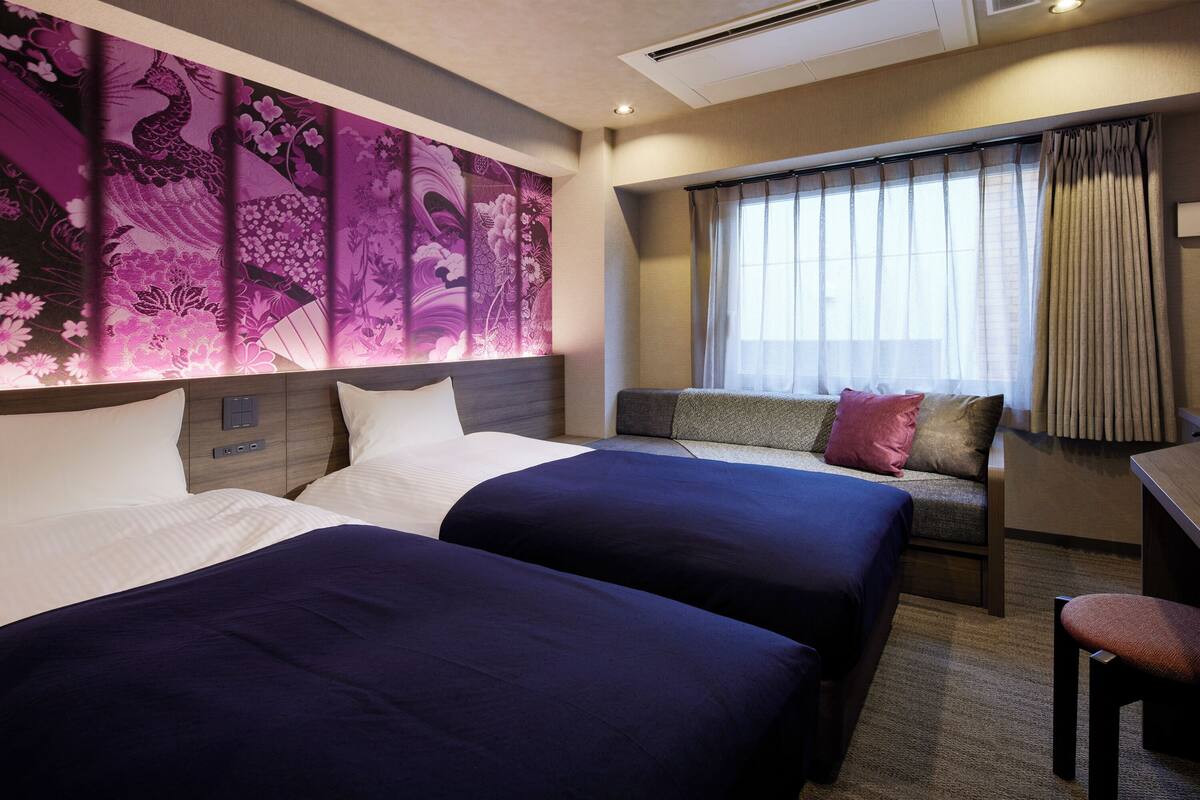 Een hotelkamer met twee bedden, een bureau en een raam met gordijnen.