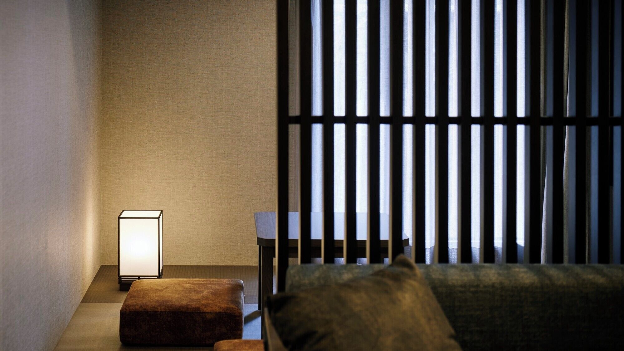 A room with a bed, a nightstand with a lamp, a window with vertical blinds, and a textured wall.