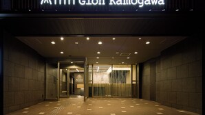 The entrance to the Minn Gion Kamogawa hotel with a modern design, featuring a prominent illuminated sign, a reception area, and a tiled floor.