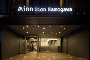 The entrance to the Minn Gion Kamogawa hotel with a modern design, featuring a prominent illuminated sign, a reception area, and a tiled floor.