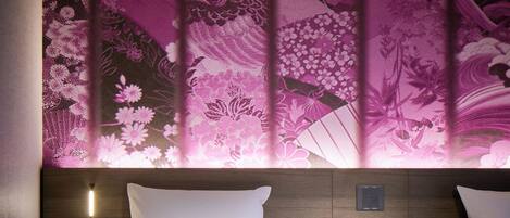 A hotel room with a bed, a nightstand, and a wall with floral wallpaper.