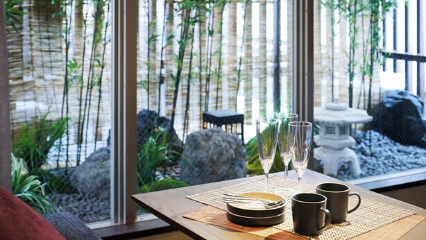 A dining table with a view of a bamboo garden through a window.