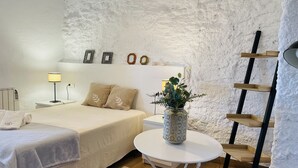 Quarto com cama, mesa de cabeceira, luminária e uma pequena mesa branca com uma planta.