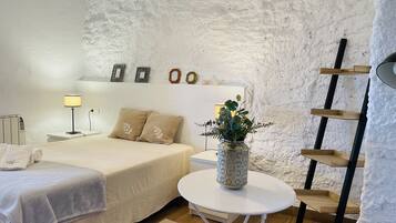 Een slaapkamer met een bed, nachtkastje, lamp en een kleine witte tafel met een plant.