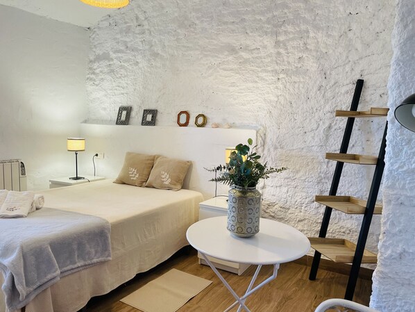 Een slaapkamer met een bed, nachtkastje, lamp en een kleine witte tafel met een plant.