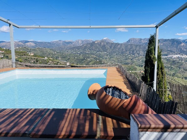 Ein Pool mit Blick auf Berge, eine Holzterrasse und ein Pergola-Gebilde.