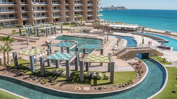 A resort with multiple swimming pools, sun loungers, and a view of the ocean.