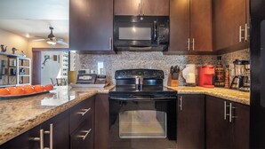 A modern kitchen with dark wooden cabinets, a stainless steel microwave, a black stove, and granite countertops.
