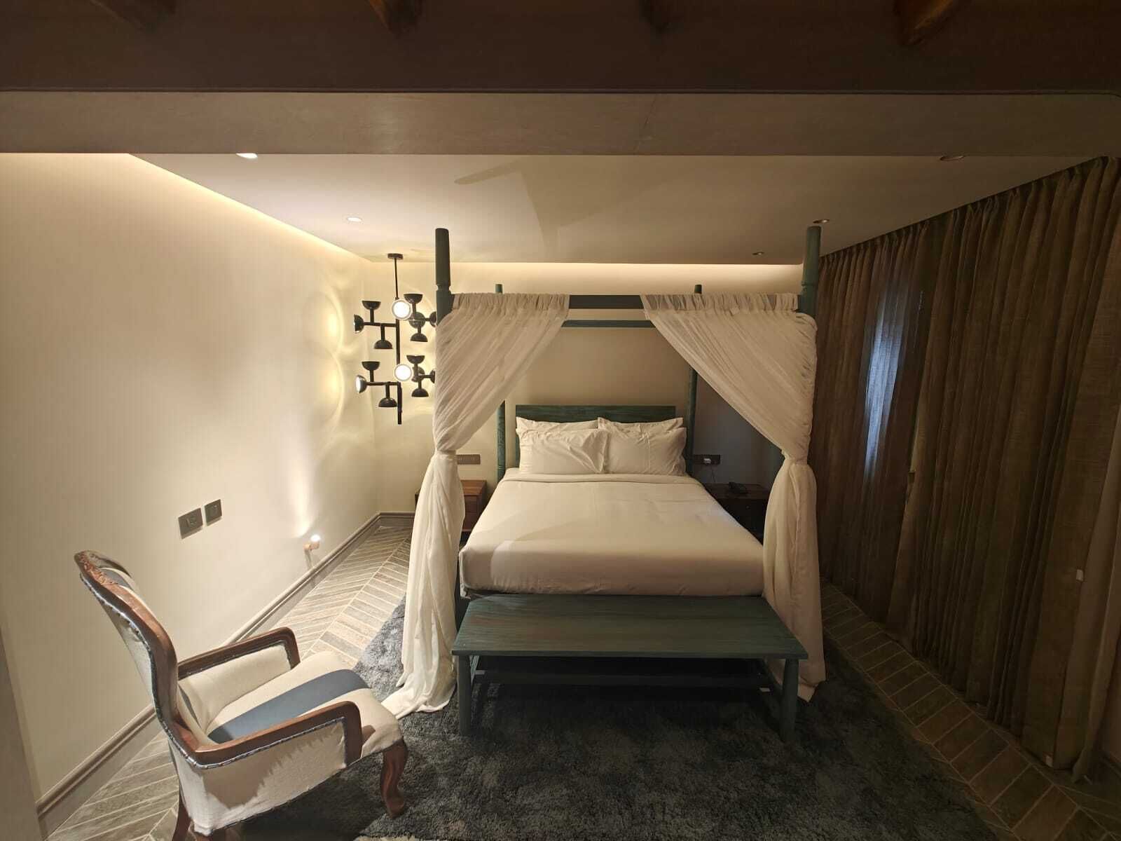 Une chambre à coucher comprenant un lit, une chaise, une table de chevet et un luminaire fixé au mur.