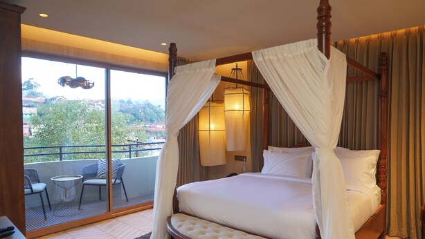 A four-poster canopy bed with a view of a balcony and cityscape. - Maison de Zen (Ooty)