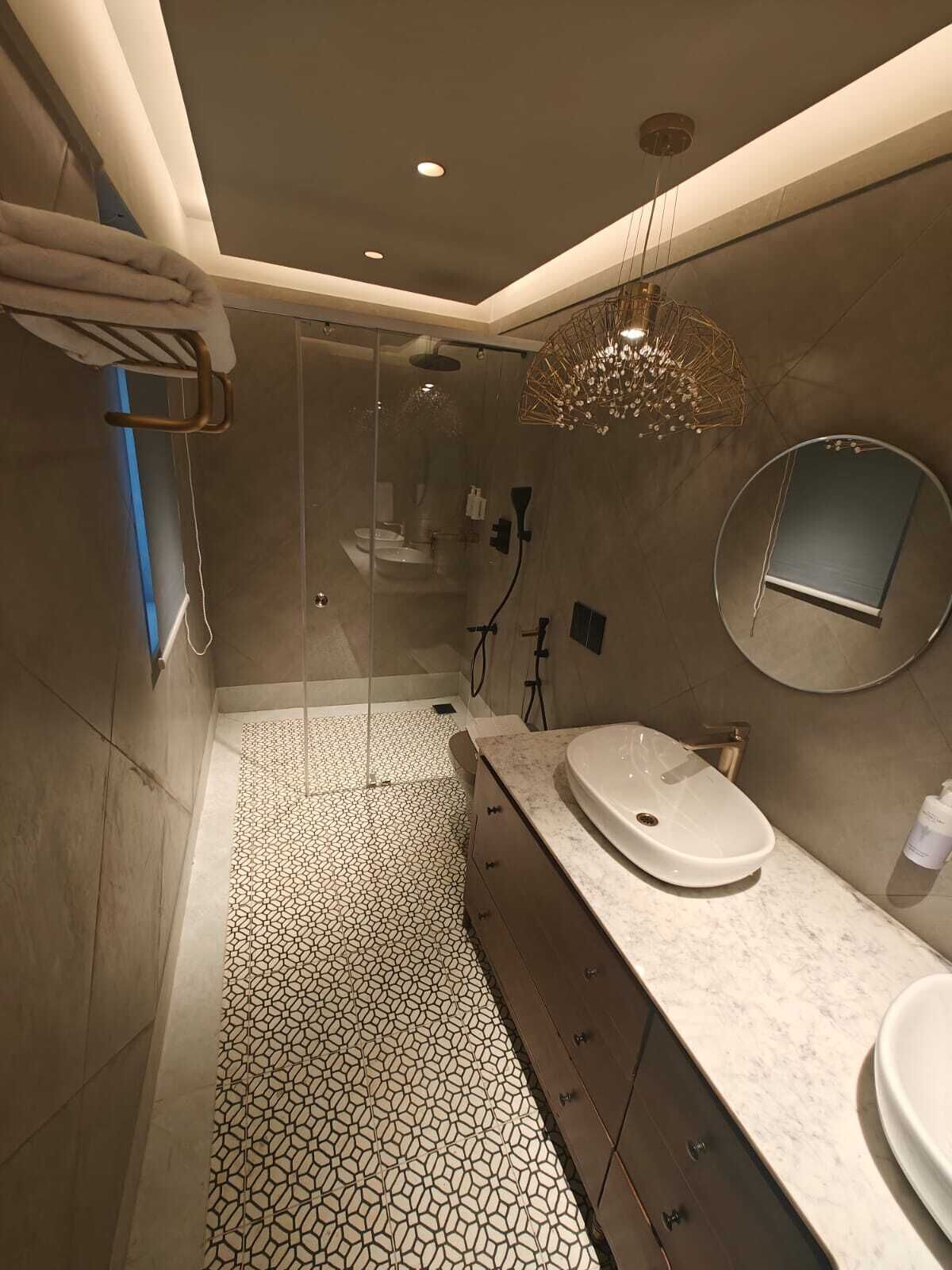 Une salle de bain moderne avec une douche à parois de verre, un meuble-lavabo doté d’un miroir rond et un carrelage à motifs.