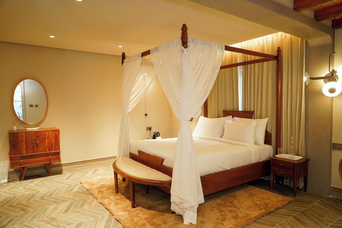 Quarto com cama de dossel, mesa de cabeceira de madeira, espelho e piso com padrão herringbone.