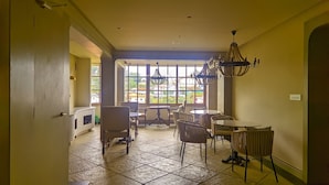 A spacious room with a large window, a chandelier, and a dining area with chairs and a table. - Maison de Zen (Ooty)