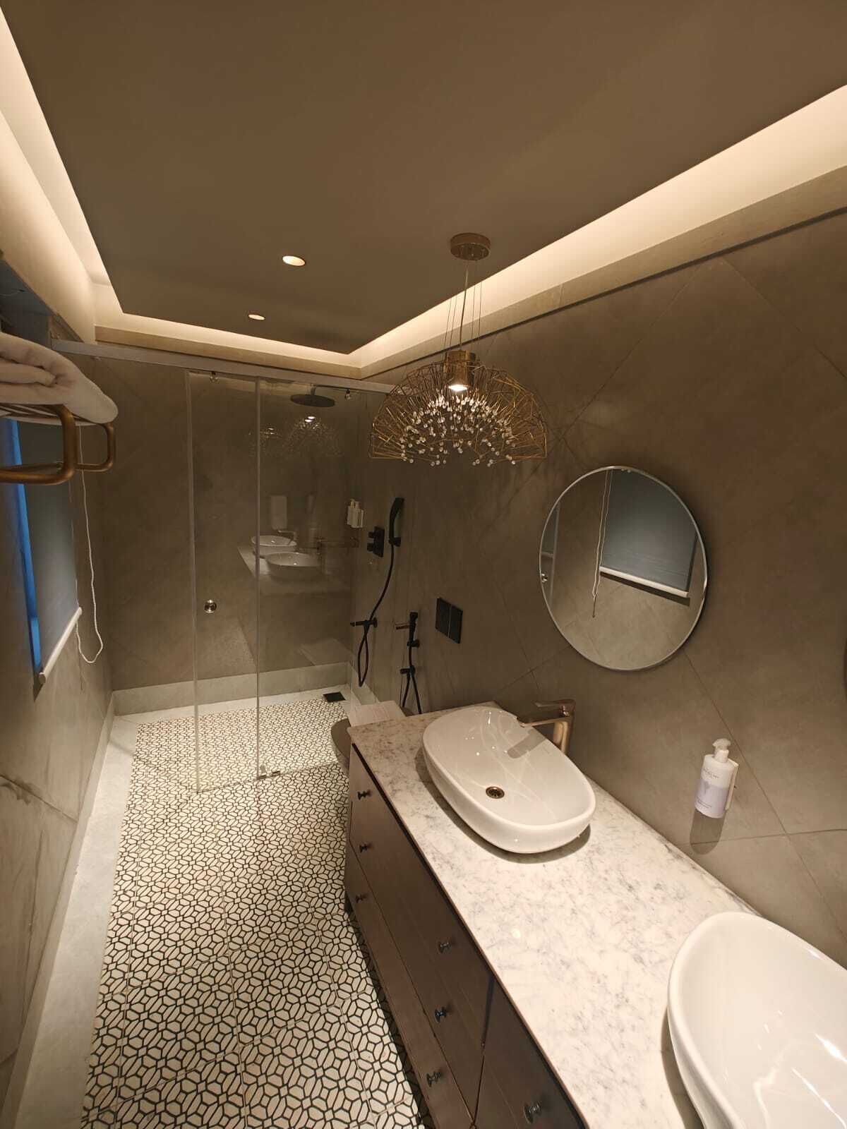 Un baño moderno con ducha envuelta en vidrio, un espejo redondo y tocador de mármol.