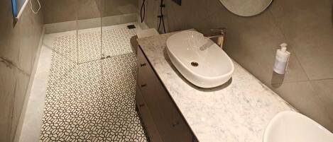 Un baño moderno con ducha envuelta en vidrio, un espejo redondo y tocador de mármol.