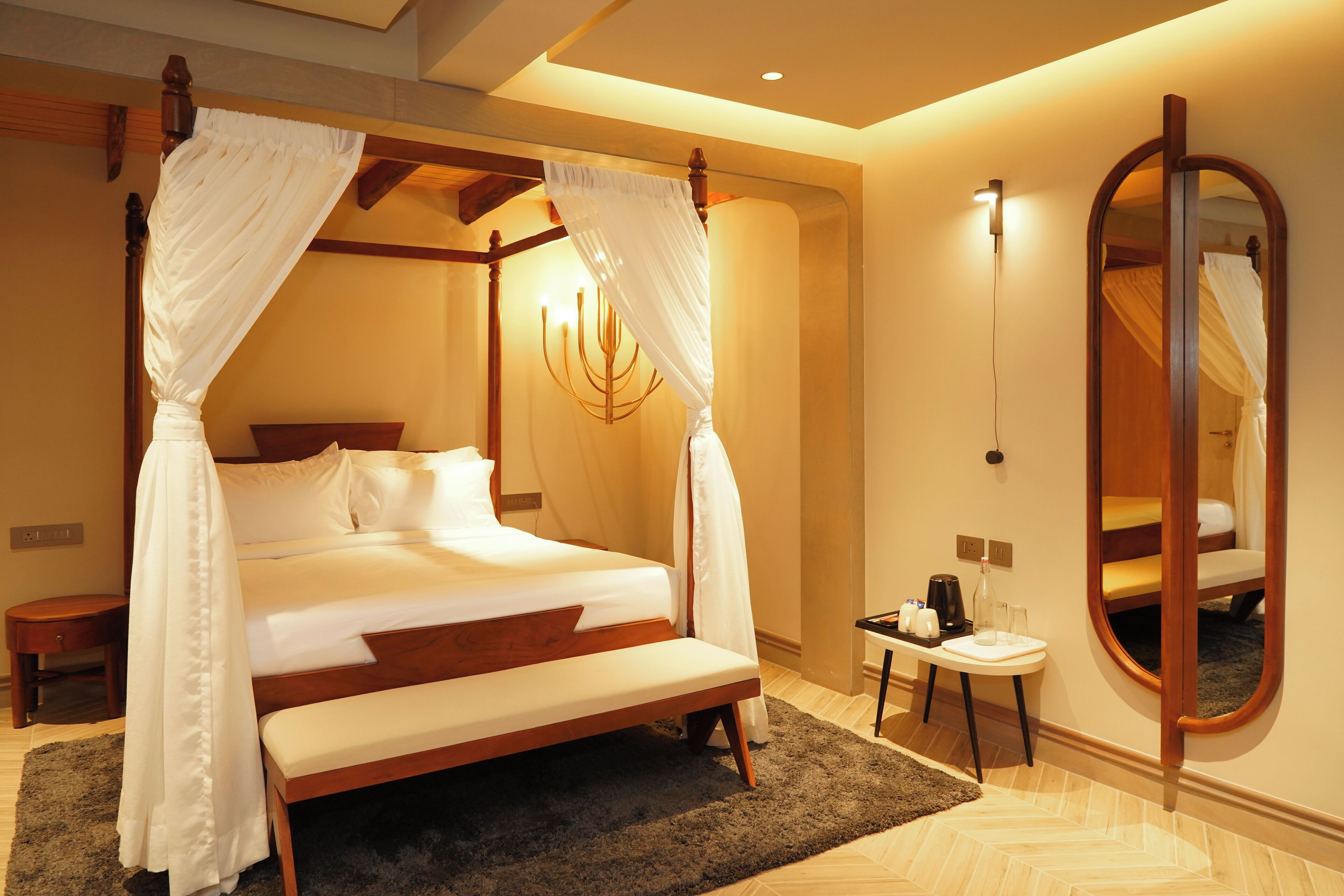 A four-poster canopy bed with a bench, bedside table, and a mirror.