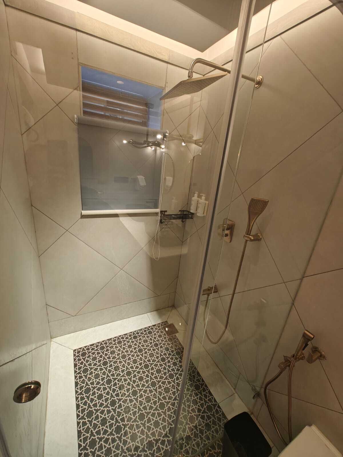 A modern shower area with a glass enclosure, a small window, and a patterned floor.