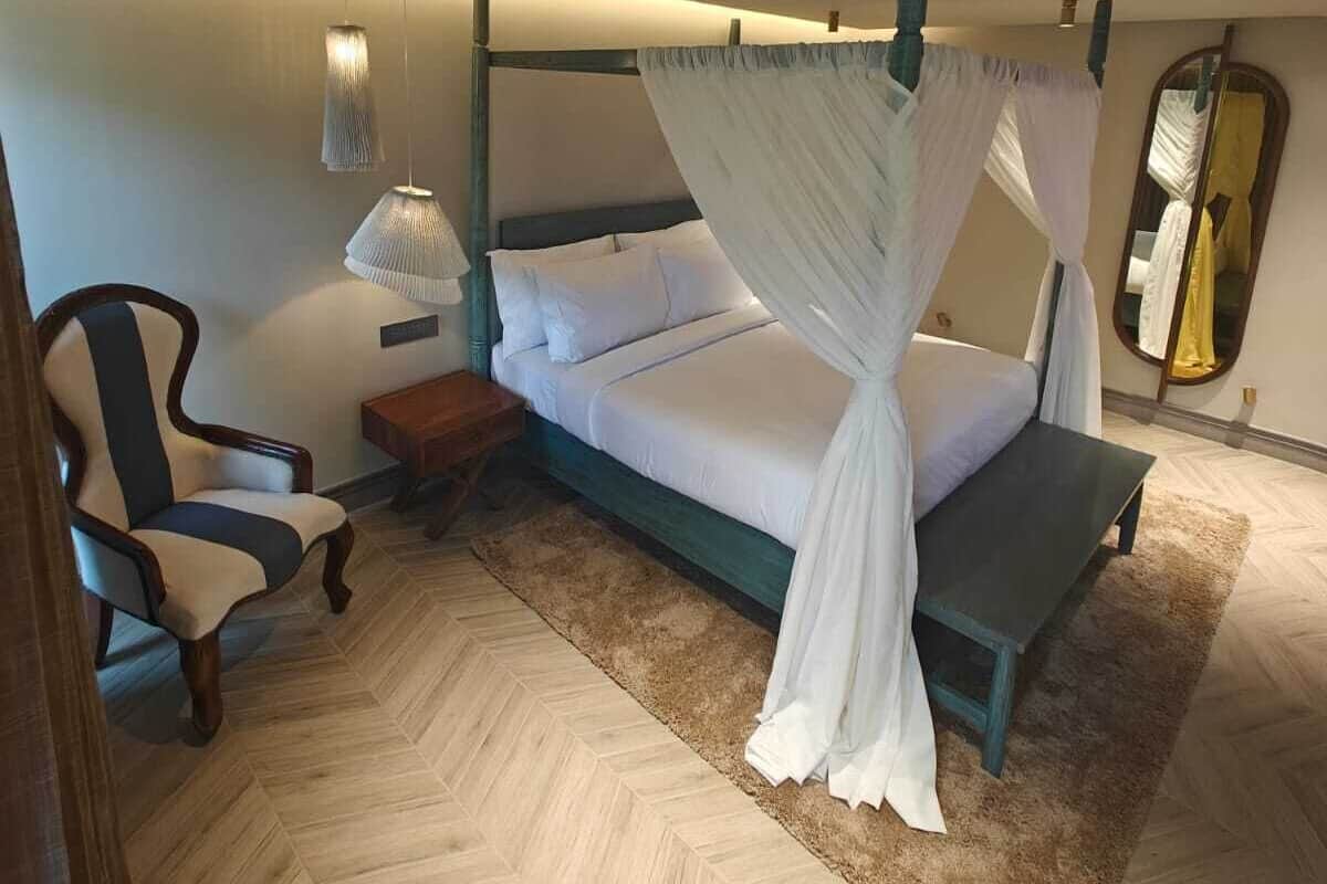 Quarto com cama de dossel, uma cadeira, mesa de cabeceira e espelho.