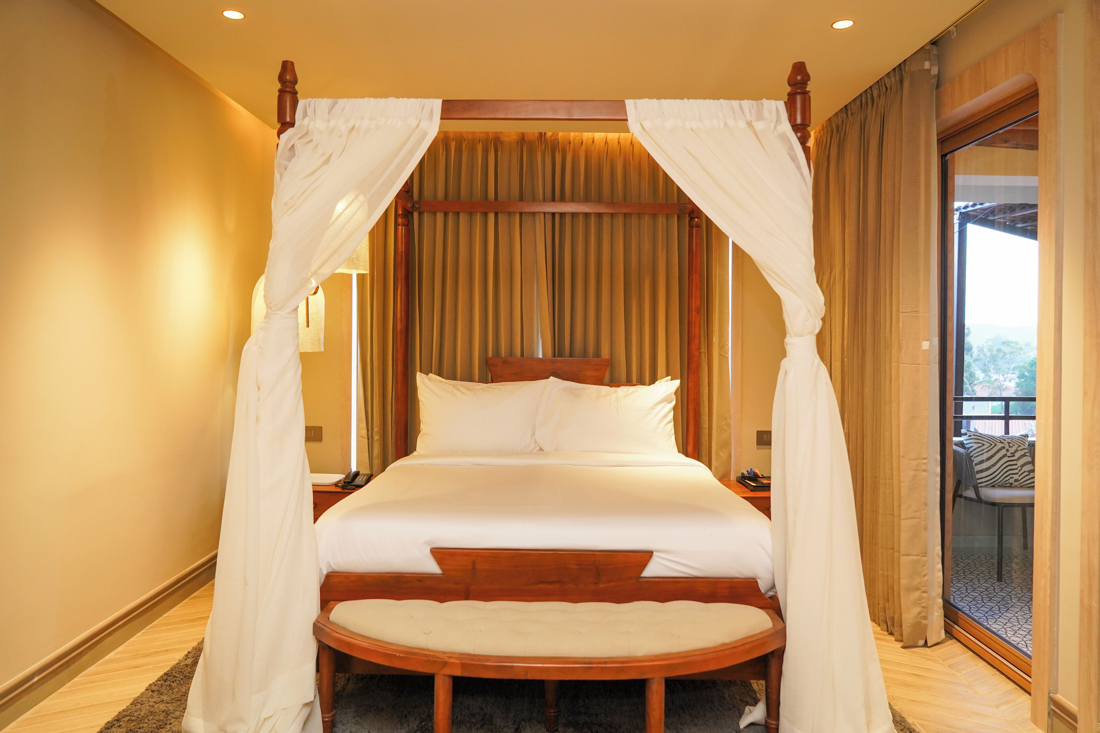 A large bed with a canopy, a round chair, and a view of the outdoors through a glass door.