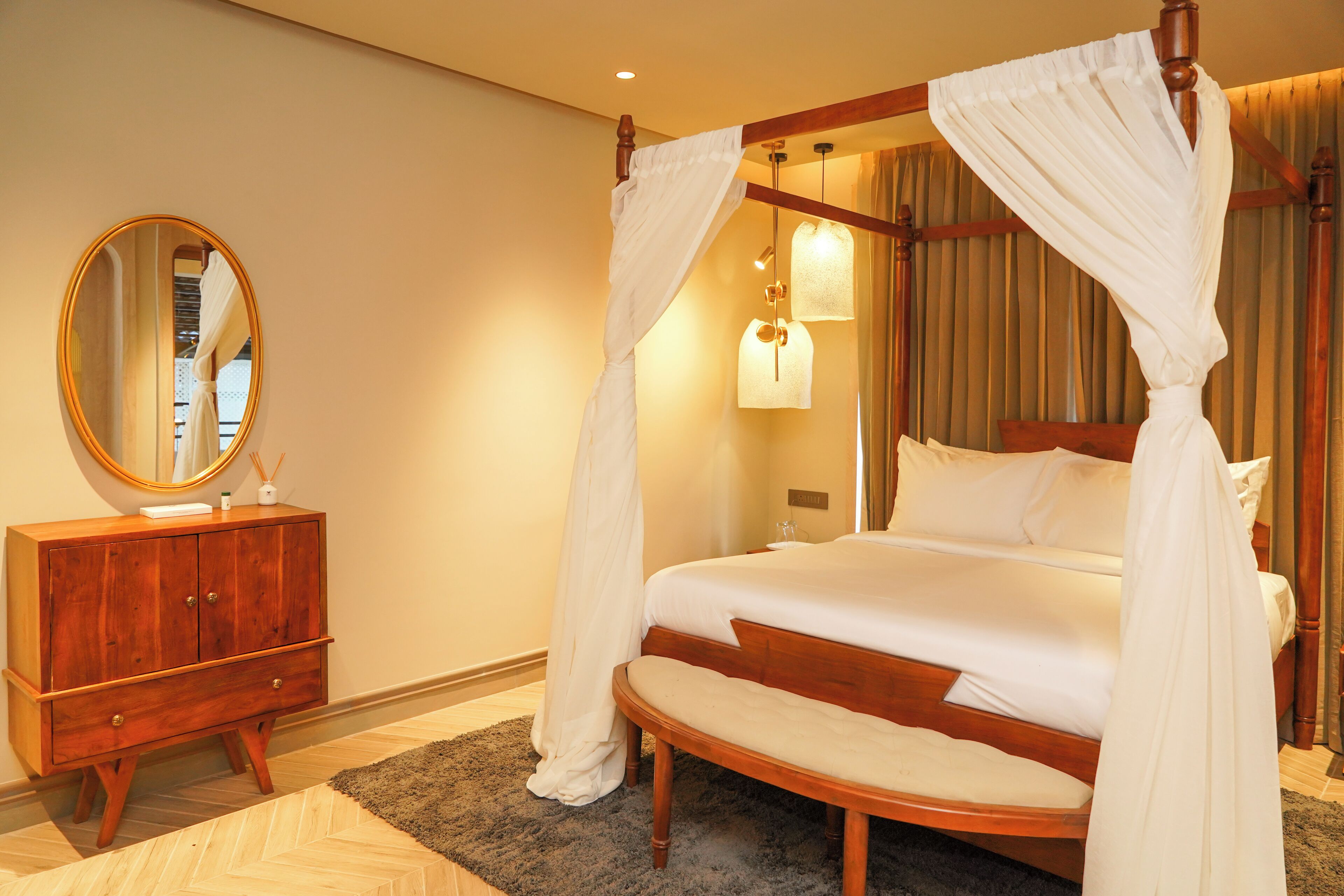 A bedroom with a four-poster canopy bed, a wooden dresser, and a round mirror.