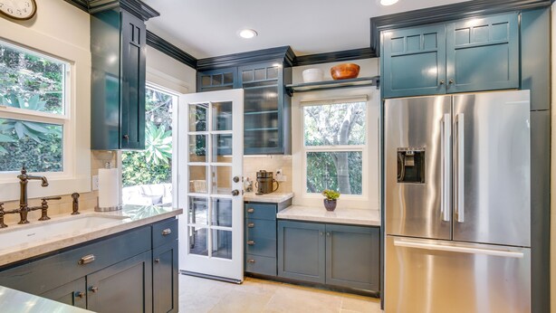 Una cocina moderna con armarios azul oscuro, electrodomésticos de acero inoxidable y una ventana con vistas a la vegetación.