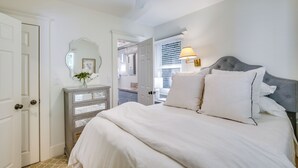 Un dormitorio con cama, cómoda, espejo, ventilador de techo y ventana con persianas.