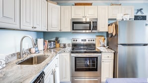A kitchen with white cabinets, stainless steel appliances, a marble countertop, and a ceiling fan. - Scenic Oceanfront Condo in Myrtle Beach! (Myrtle Beach)