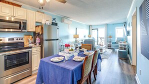 A modern kitchen with stainless steel appliances, a dining area with a blue tablecloth, and a ceiling fan. - Scenic Oceanfront Condo in Myrtle Beach! (Myrtle Beach)