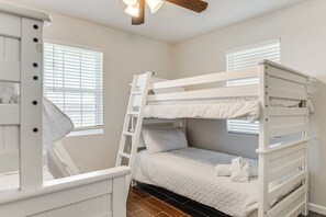 Een slaapkamer met een stapelbed, een ladder, wit beddengoed en twee ramen met zonwering.