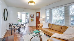 A living room with a glass coffee table, a brown leather sofa, and a dining area with a glass table and chairs.
