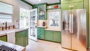 A kitchen with green cabinets, a stainless steel refrigerator, and a window with a view of greenery.