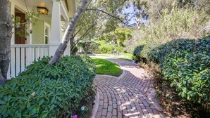 A brick pathway leading to a house with a porch, surrounded by well-maintained hedges and trees.