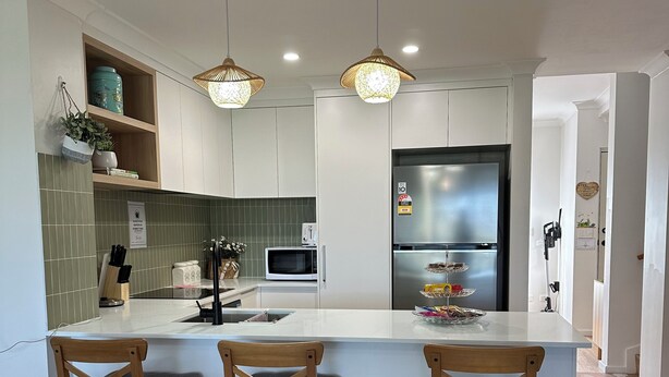 Een moderne keuken met een centraal eiland, houten stoelen, een koelkast en hangende verlichting.