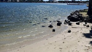 Een strand met helder water, een zandstrand en gebouwen op de achtergrond.