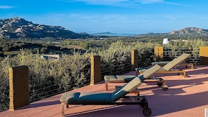 Eine Terrasse mit Liegestühlen mit Blick auf eine gebirgige Landschaft.