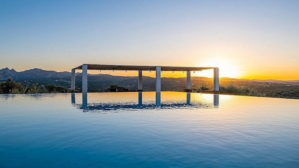 Ein Infinity-Pool mit einer Pergola, umgeben von einer Berglandschaft bei Sonnenuntergang.