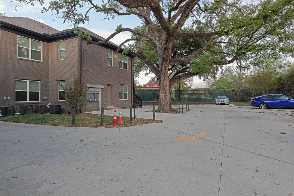 A parking lot with a building, a tree, and a blue car.