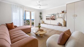 A modern living room with a sofa set, a coffee table, a TV mounted on the wall, and a balcony with a view. - Bright 2-Bed Apartment with Stunning Ocean Views (Kings Beach)