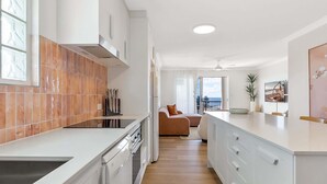 A modern kitchen with white cabinetry, a built-in oven, and a dining area with a view. - Bright 2-Bed Apartment with Stunning Ocean Views (Kings Beach)