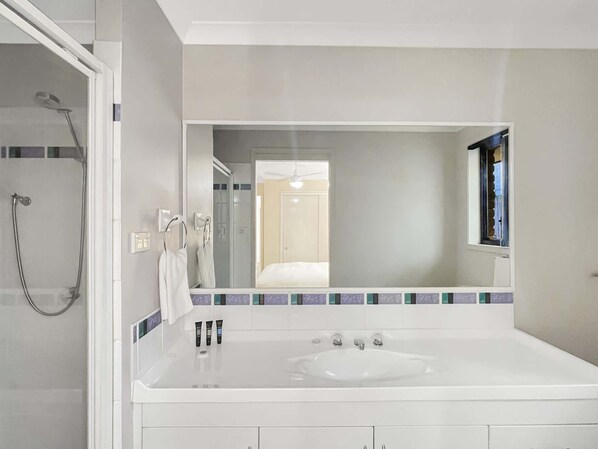 A modern bathroom with a large mirror, a bathtub, and a shower.