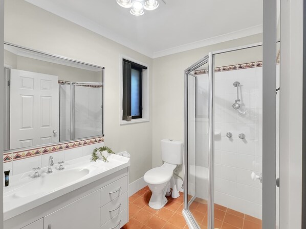 Une salle de bain avec un lavabo blanc, un miroir, des toilettes et une douche en verre.